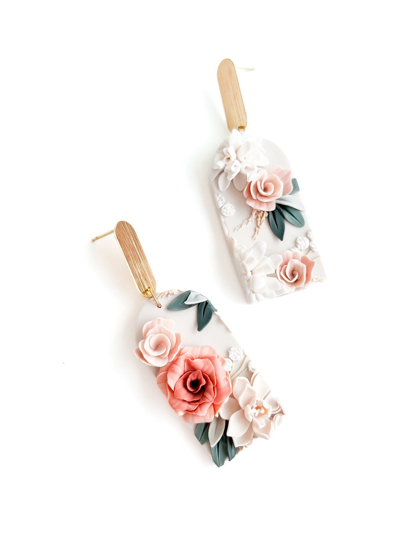 The Harper earrings by Agave Designs are handmade from polymer clay with gold-plated hooks, featuring unique 3D floral designs in pink, coral, white, and green on a pale base. Each pair is made to order for a personalized touch.
