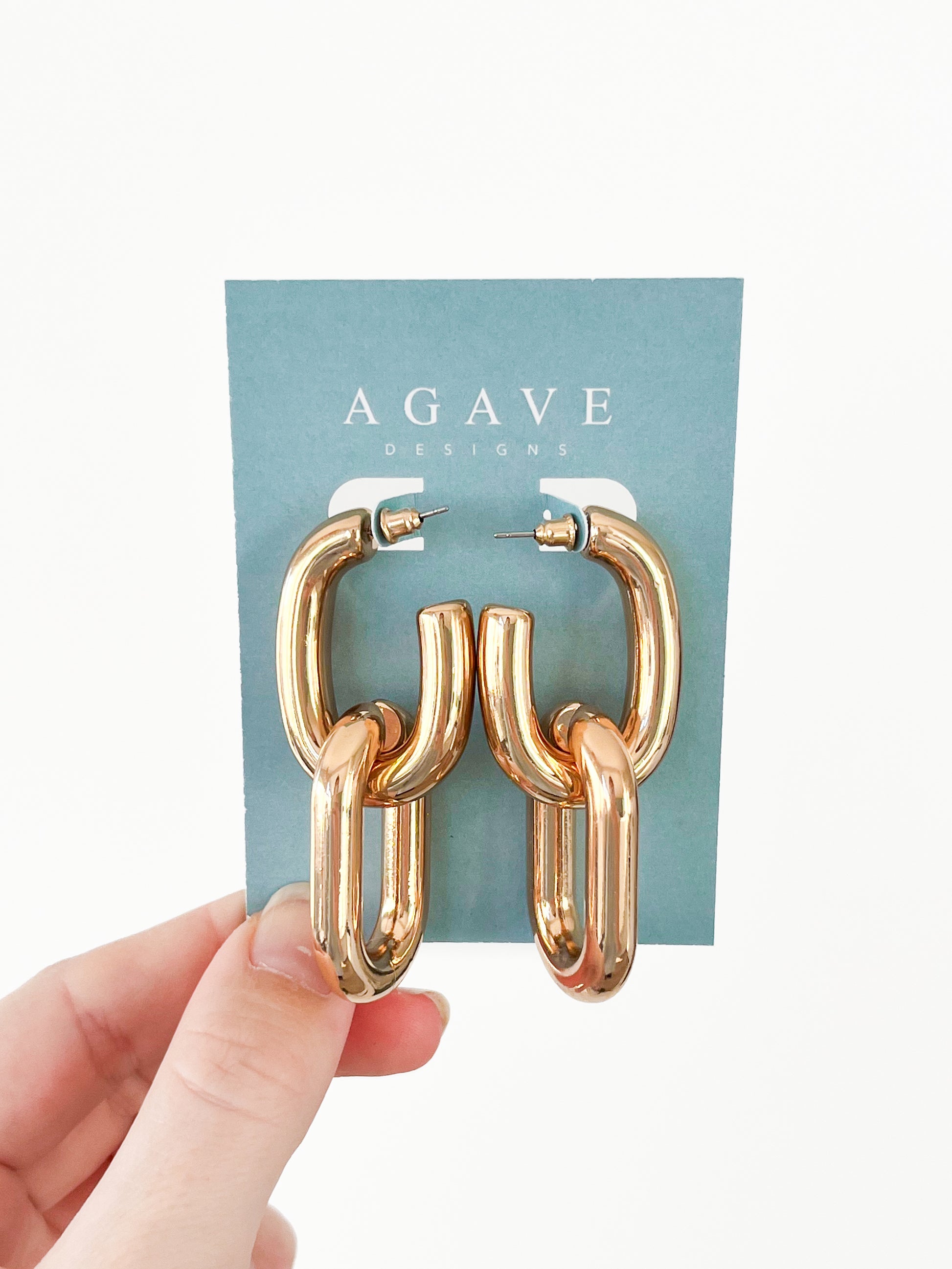 A hand displays a card featuring the Link Hoops, a pair of chunky gold chain-link earrings made from zinc alloy by Agave Designs, set against a plain white background.