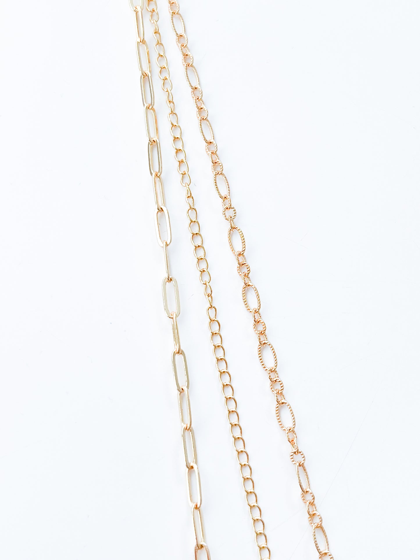Four delicate gold chains from Agave Designs' 3 Tiered Necklace set are laid out parallel to each other against a white background. The shortest part measures 55cm, and the chains range from larger, elongated links to smaller, rounded links, showcasing a variety of intricate link patterns.