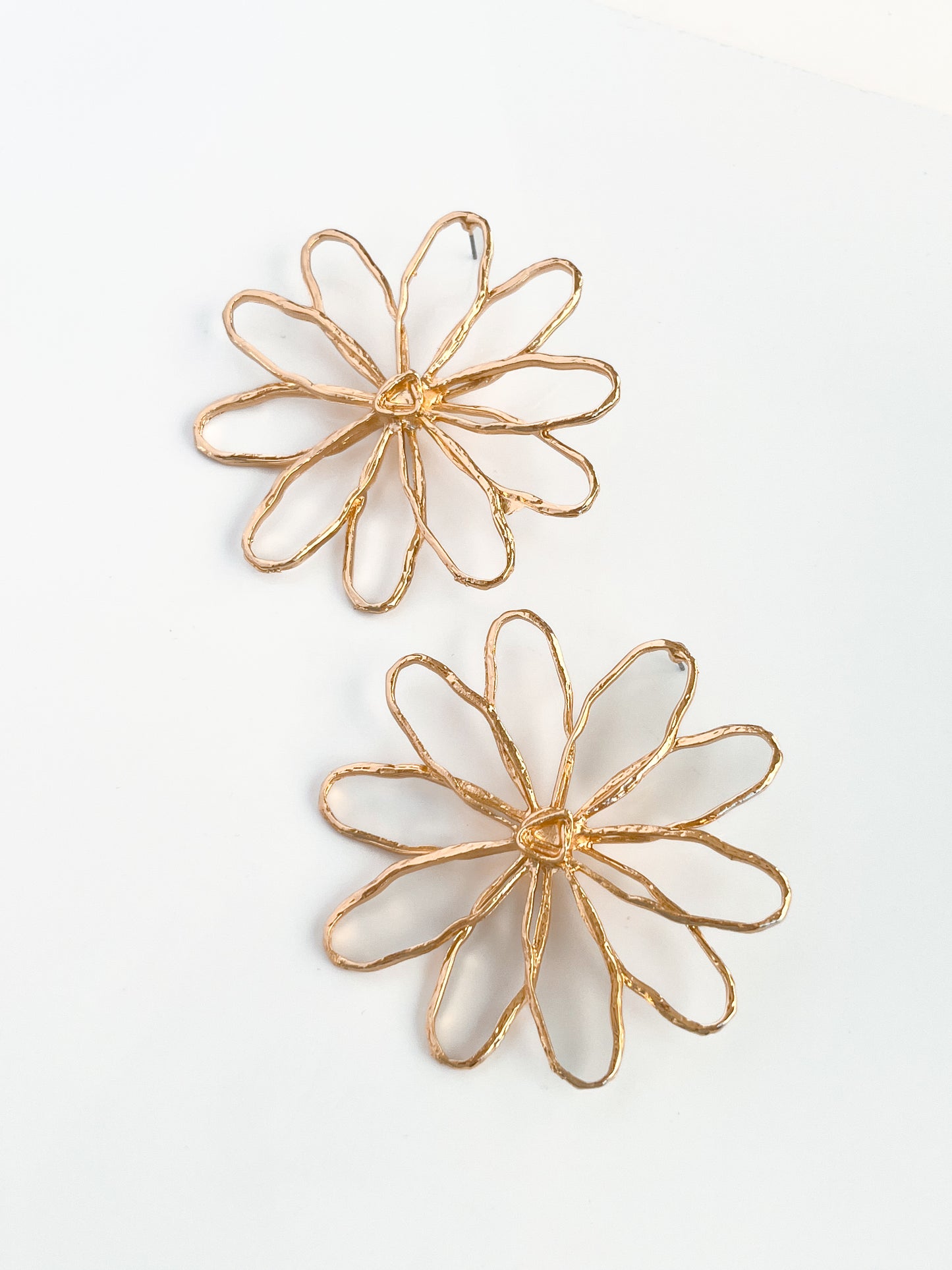 The Large Daisy Studs by Agave Designs are two gold wire earrings crafted from zinc alloy, featuring intricate petal-like loops resembling daisies on a white background.