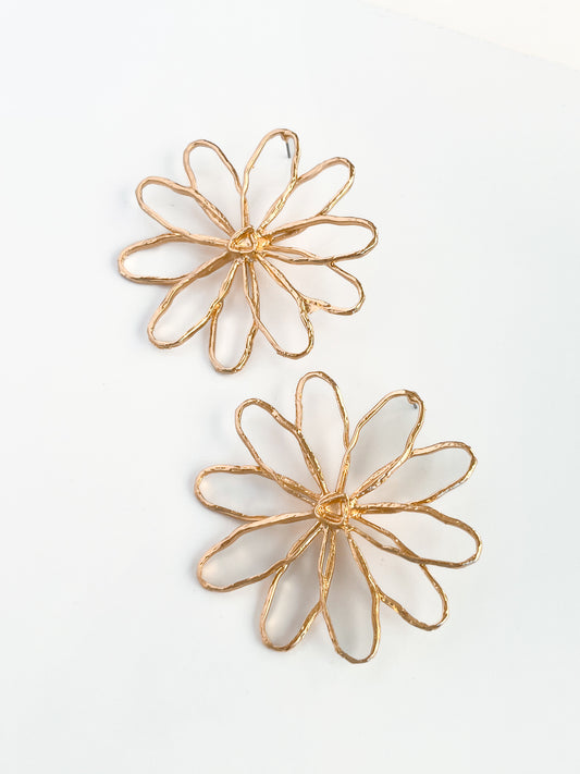 The Large Daisy Studs by Agave Designs are two gold wire earrings crafted from zinc alloy, featuring intricate petal-like loops resembling daisies on a white background.