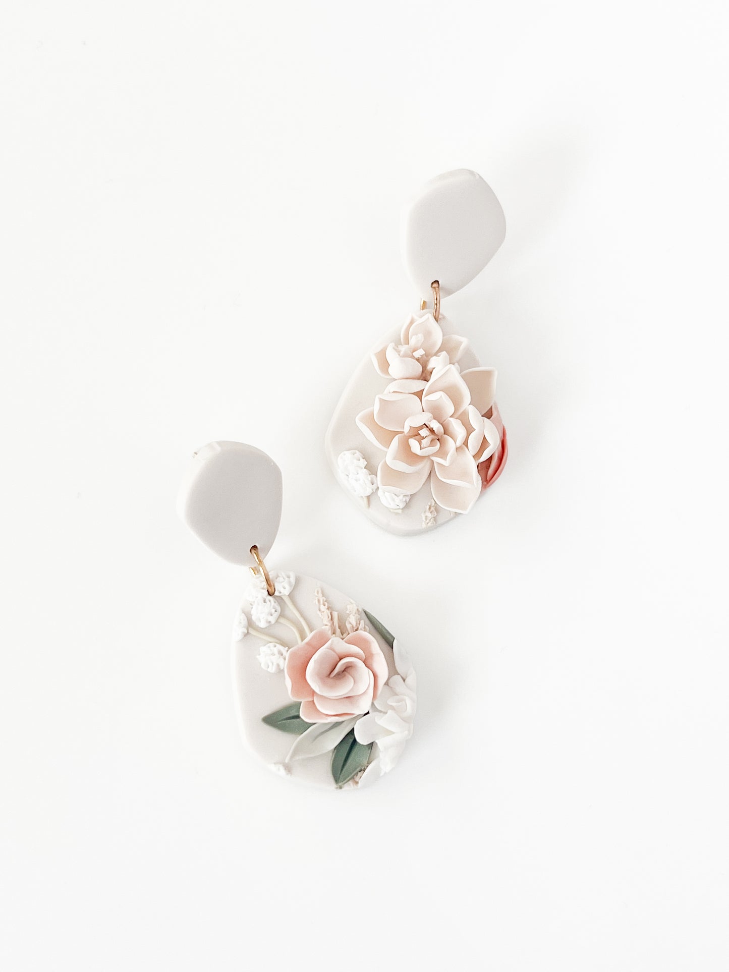 The "Tammy" earrings by Agave Designs feature white clay dangles with handcrafted pink and cream floral details, delicate leaf accents, and sterling silver hooks, displayed on a white background.