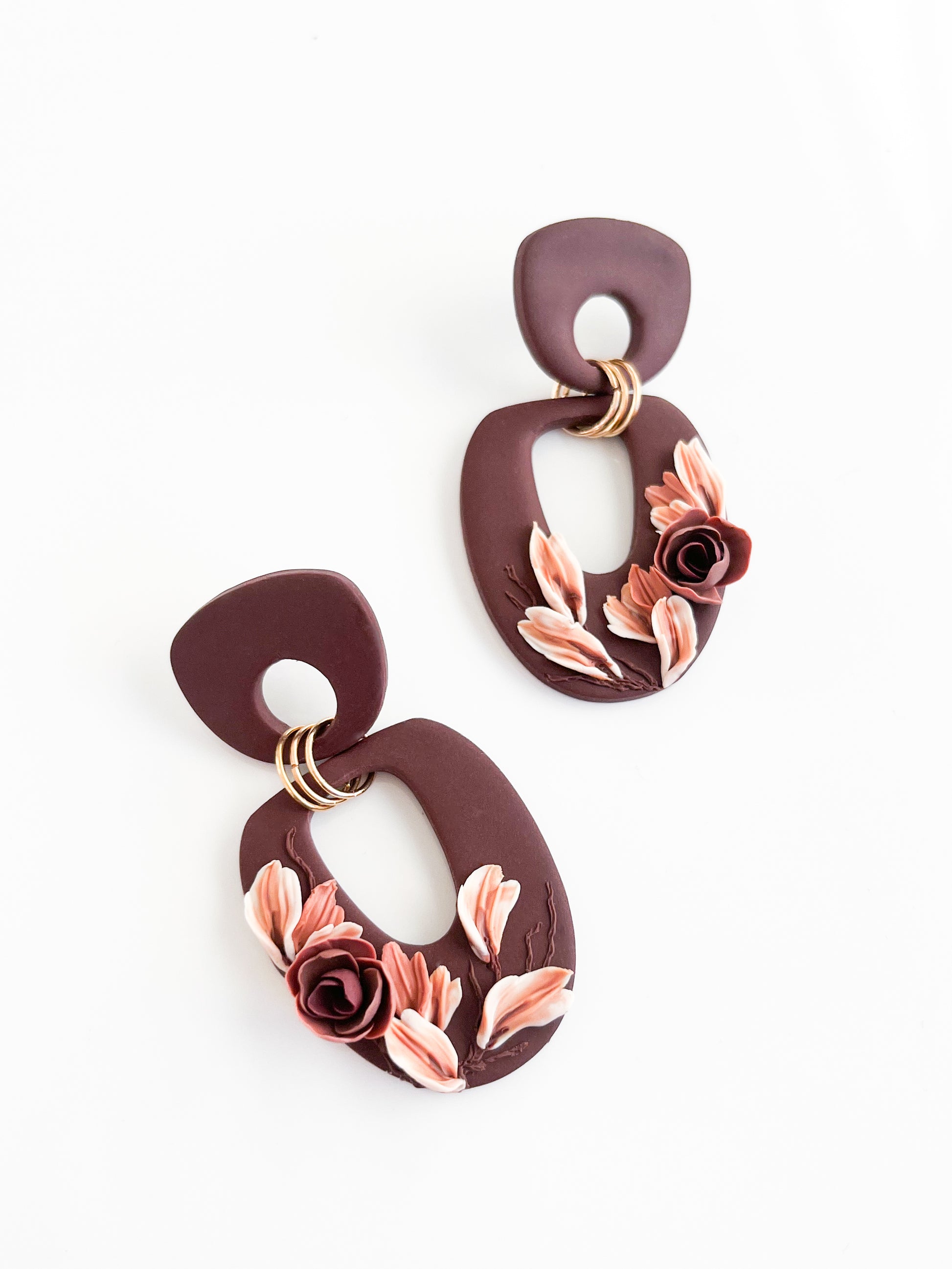 The Felicity earrings by Agave Designs feature handcrafted burgundy circles with pink and burgundy clay floral designs. Made to order, they include sterling silver rings linking uneven loops on a white backdrop.