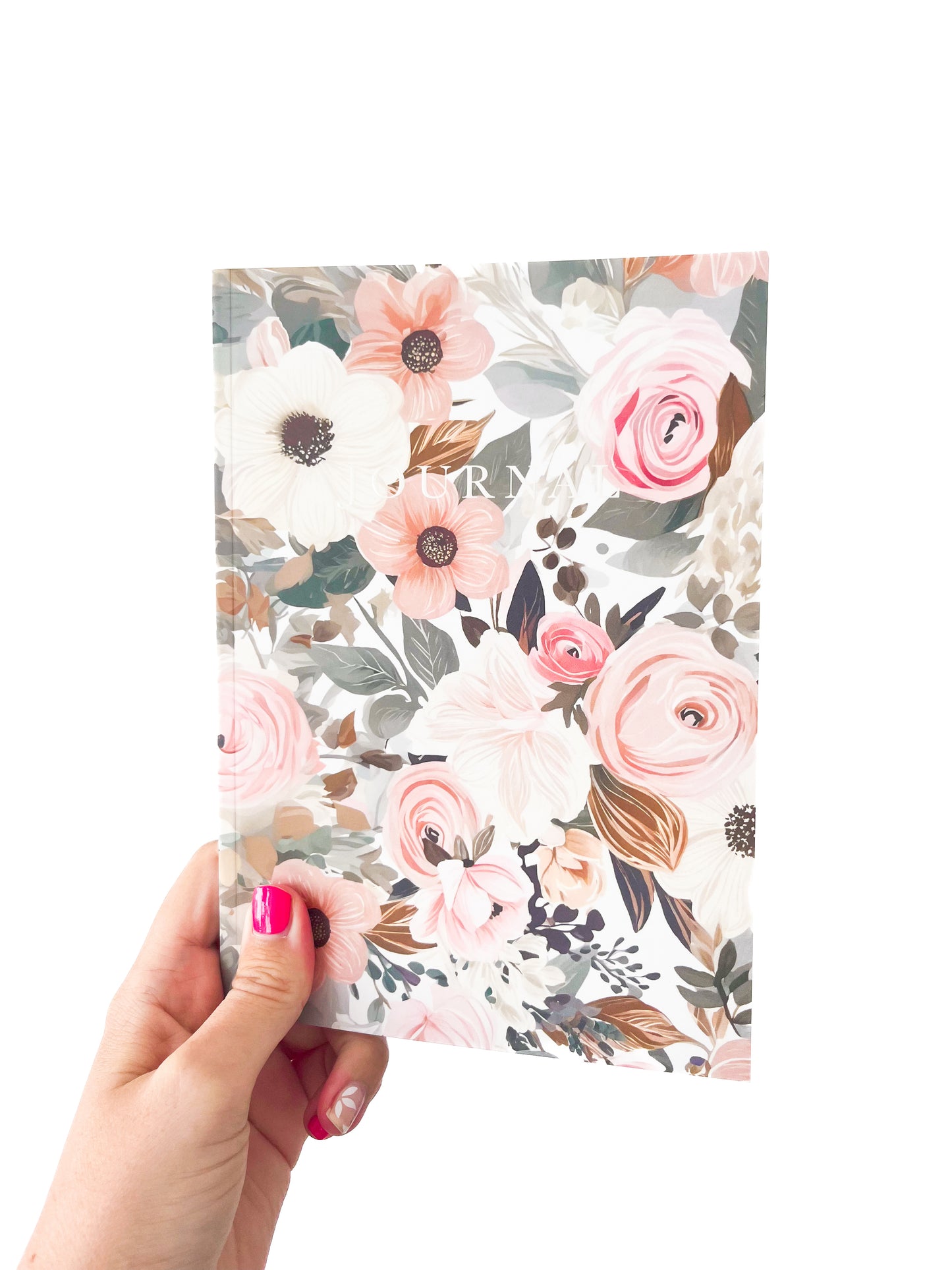 A hand with pink nail polish holds a Spring Notebook from Agave Designs. The paperback cover is adorned with large, colorful blooms in shades of pink, white, and peach along with green foliage on a light matte finish background. Inside, the lined pages await your thoughts and musings.