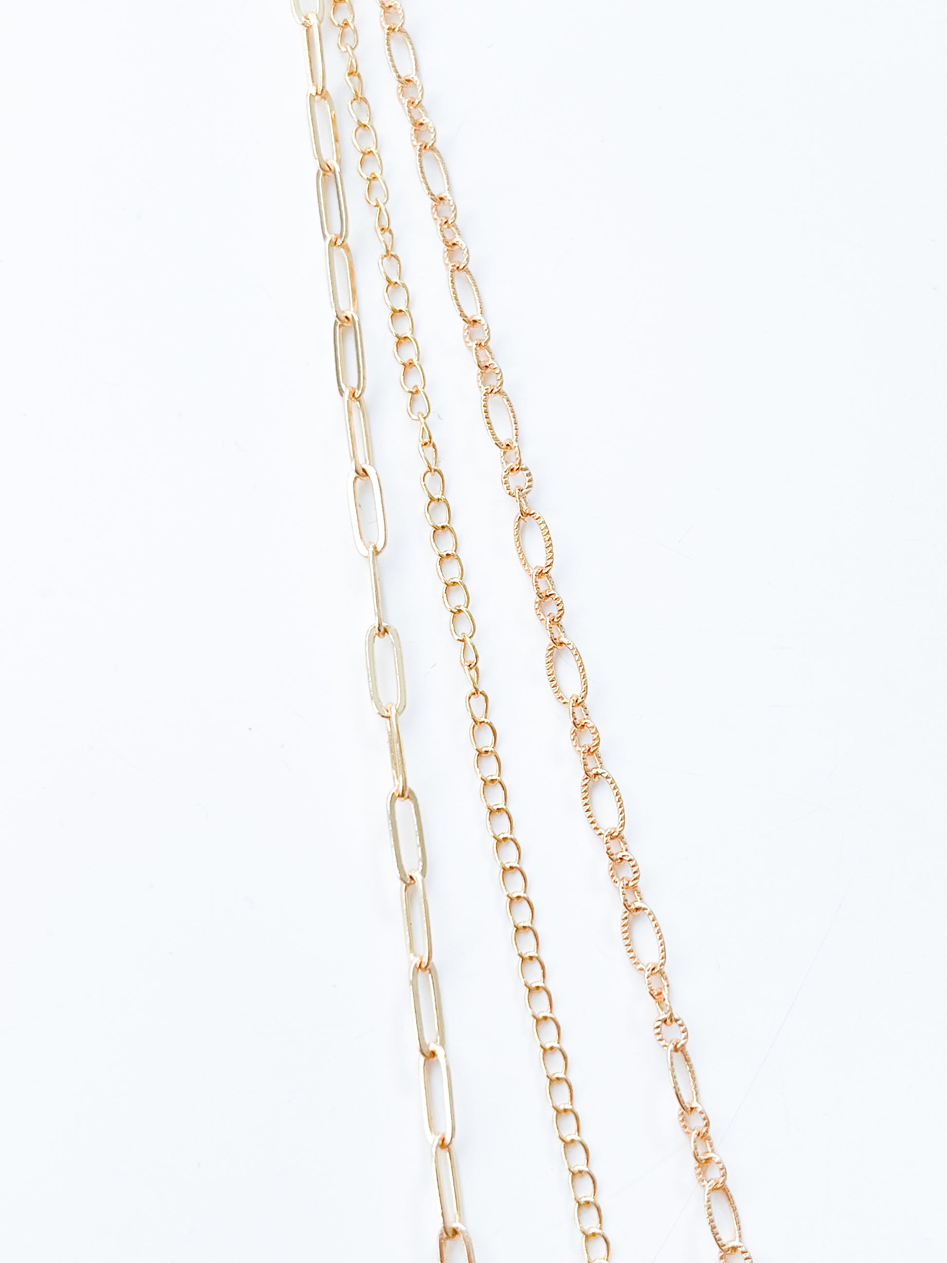 Four delicate gold chains from Agave Designs' 3 Tiered Necklace set are laid out parallel to each other against a white background. The shortest part measures 55cm, and the chains range from larger, elongated links to smaller, rounded links, showcasing a variety of intricate link patterns.