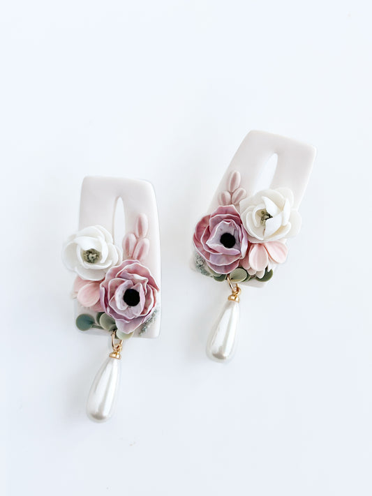 Garden Danglies by Agave Designs are elegant earrings featuring pale pink, light blue, and white floral patterns with delicate petals, green leaves, and teardrop pearl dangles on a white background.