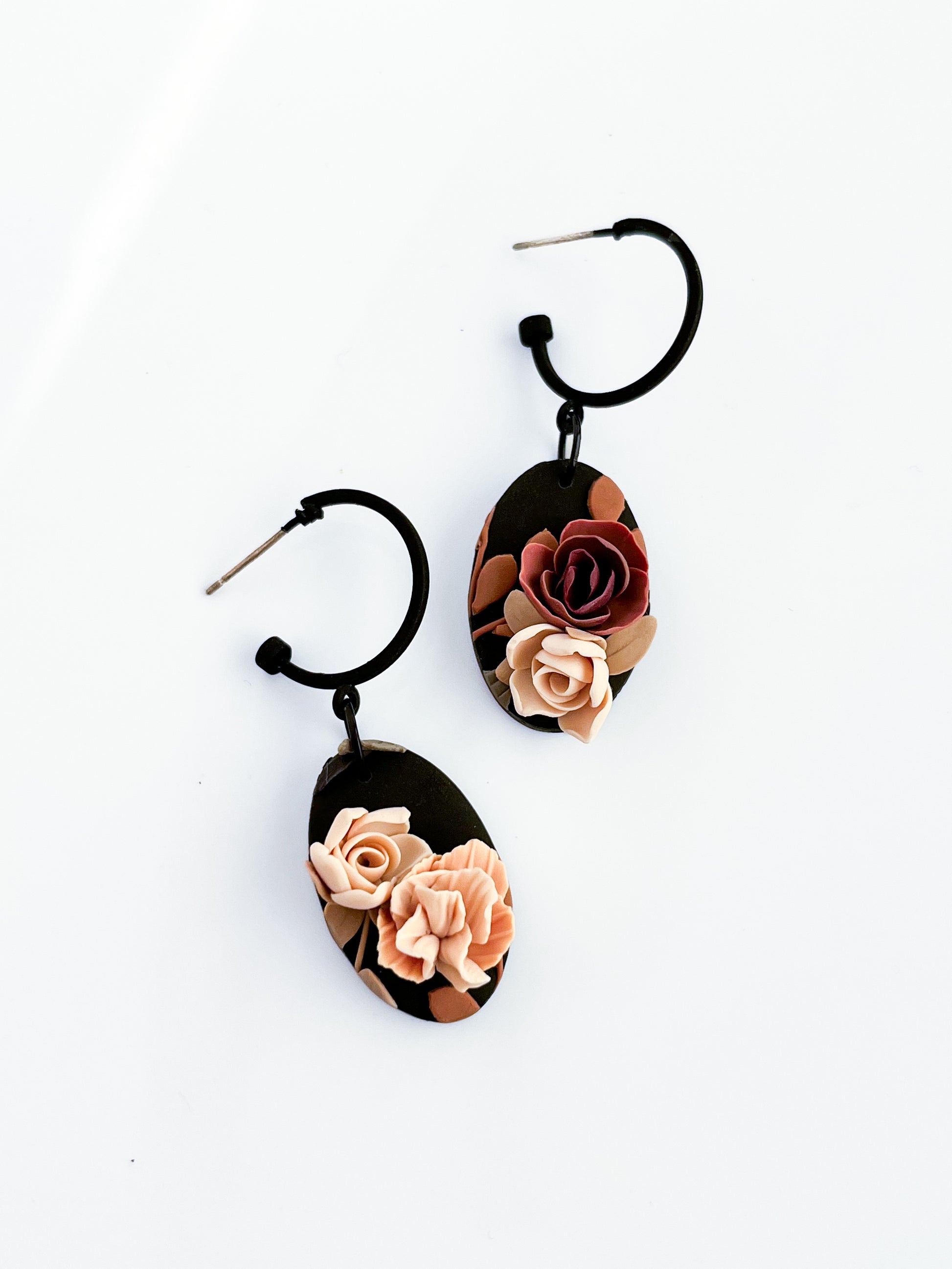 Agave Designs' Ava earrings are crafted from stainless steel with black hoops and hanging oval pendants, featuring intricate rose designs in pink and burgundy on a white background. Each made-to-order piece adds a unique touch to your accessory collection.