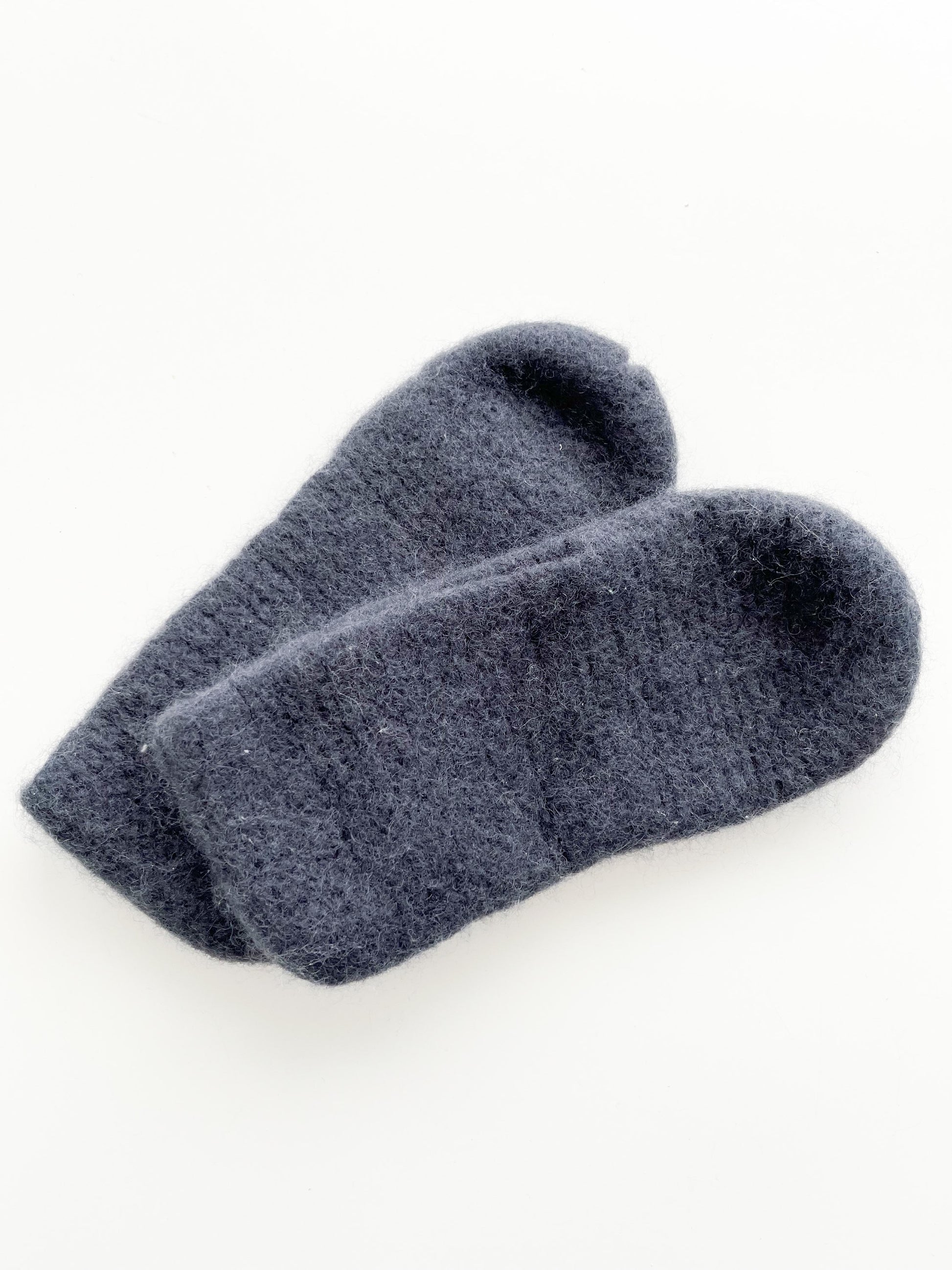 A pair of Soft Navy Wool Slippers by Agave Designs lies flat on a white background. The slippers have a soft, fuzzy texture, with one overlapping the other slightly.