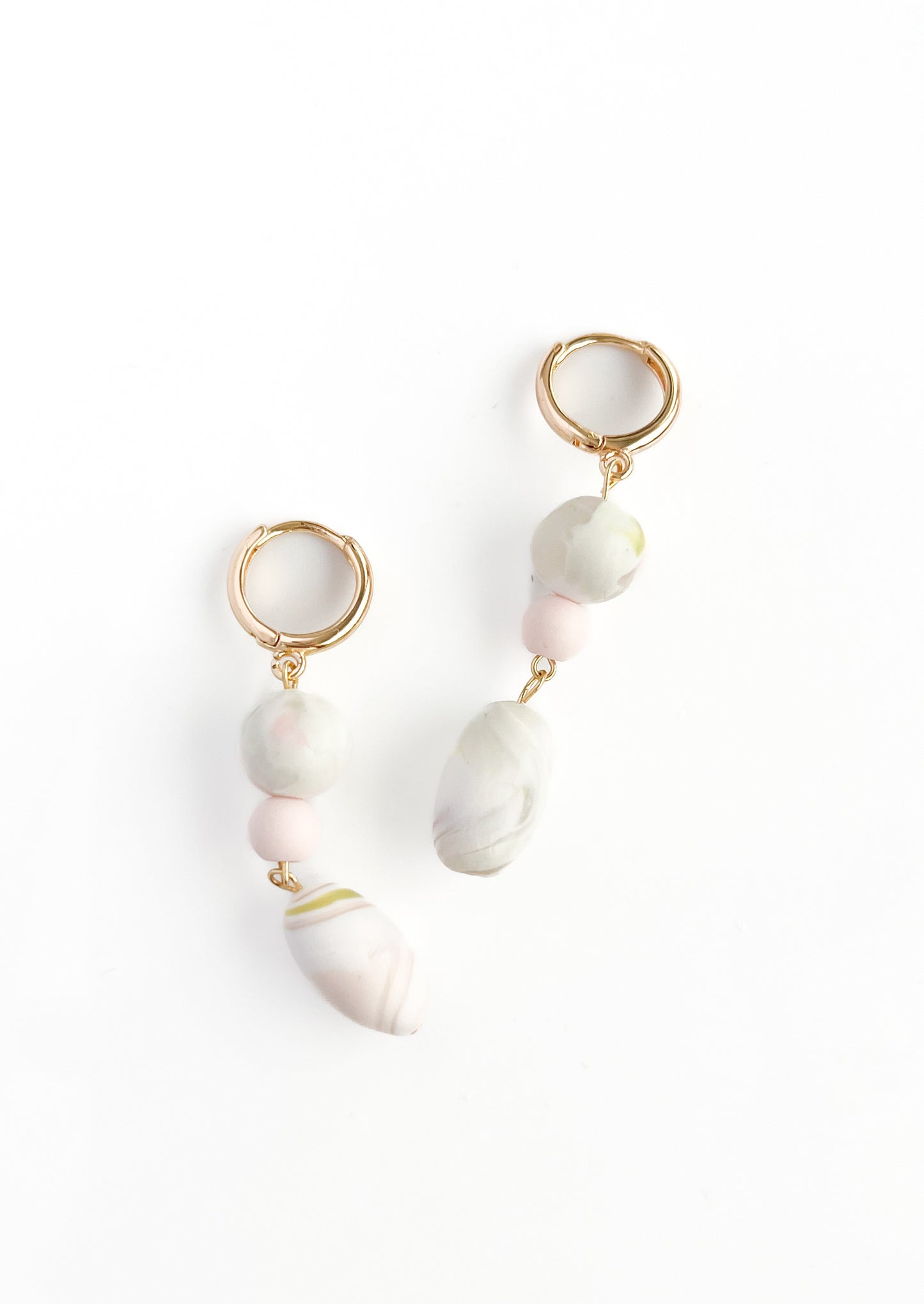 Introducing Olivia by Agave Designs: A pair of stunning gold-plated, dangling earrings with elegant hoop connectors. Each earring is adorned with three exquisite beads – a delicate small pink bead at the top, a larger marbled white and pale pink bead in the center, and an elongated marbled white and green bead at the bottom. Custom-made to perfection, these earrings measure 53mm x 10mm.