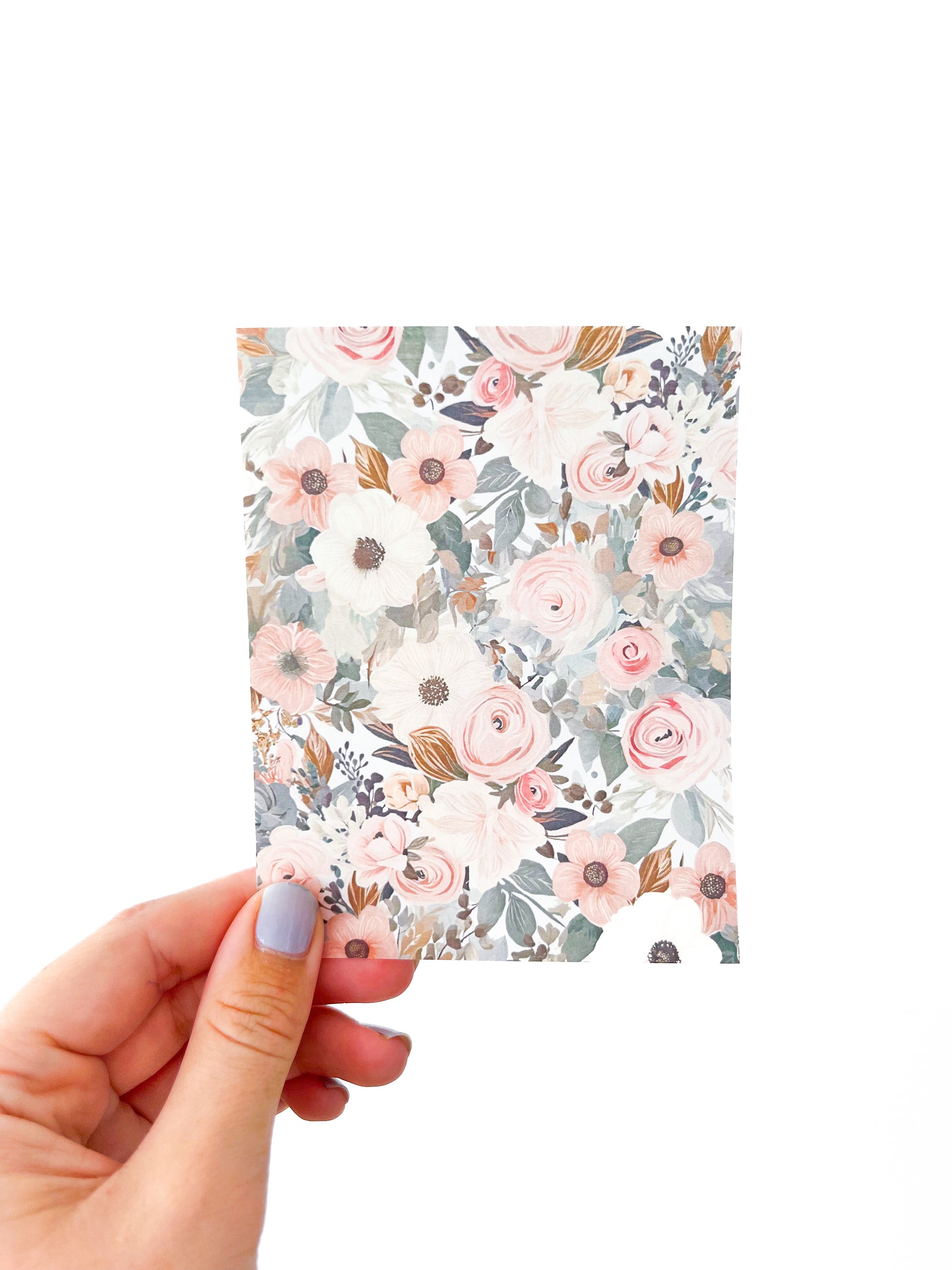 A hand with light-colored painted nails is holding a small rectangular card against a plain white background. The card, identified as the "Spring Transfer Sheet" by Agave Designs, features a floral pattern with various flowers in shades of pink, white, and peach, complemented by green leaves and subtle gray accents.